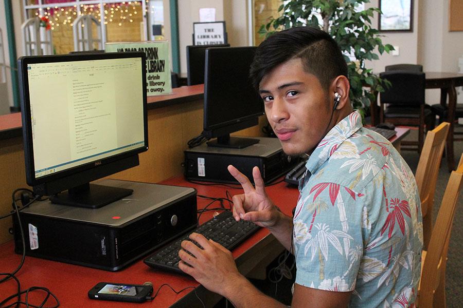 Senior Ryan Guzman throwing up a peace sign while working on an assignment in the library