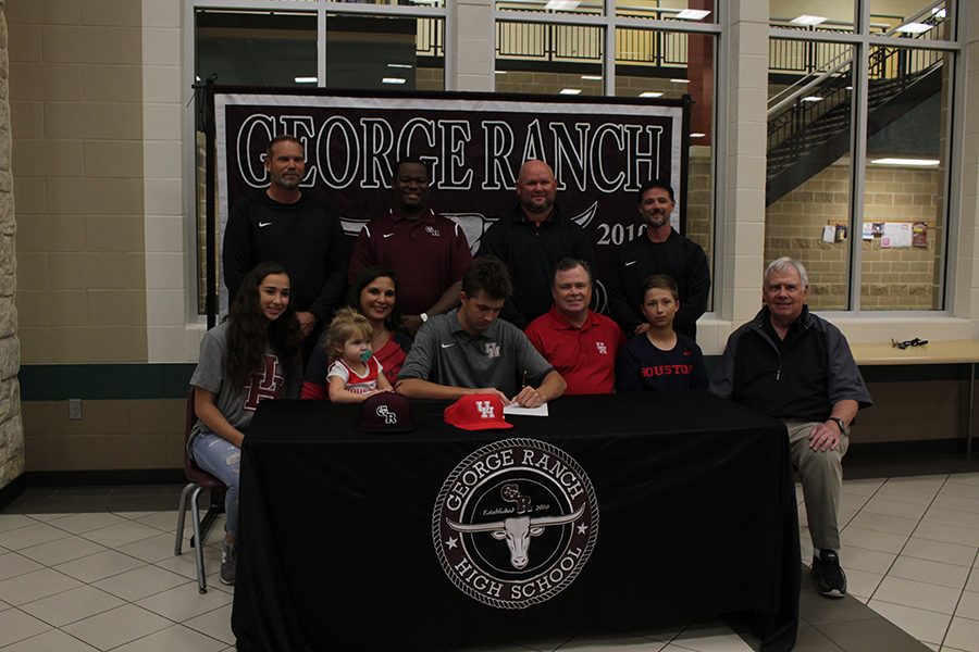 Cole McMillan sits with his family and coaches as he signs his way into collage. 