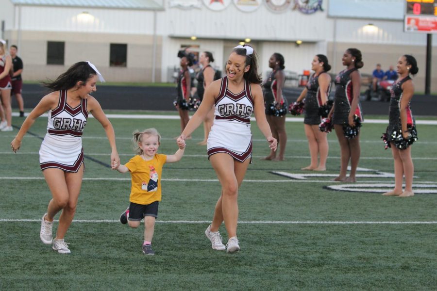 Two Lady Longhorns and a coachs daughter running along the field after the football players, preparing for the game.
