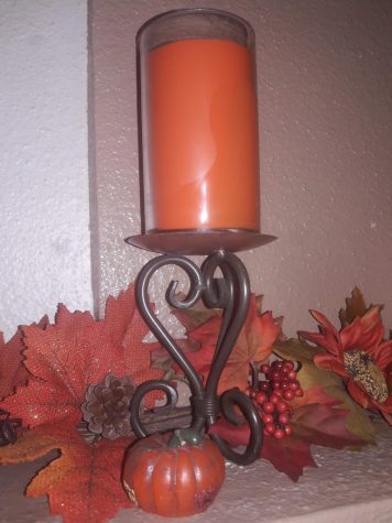 A Thanksgiving candle with fall leaves surrounding it.