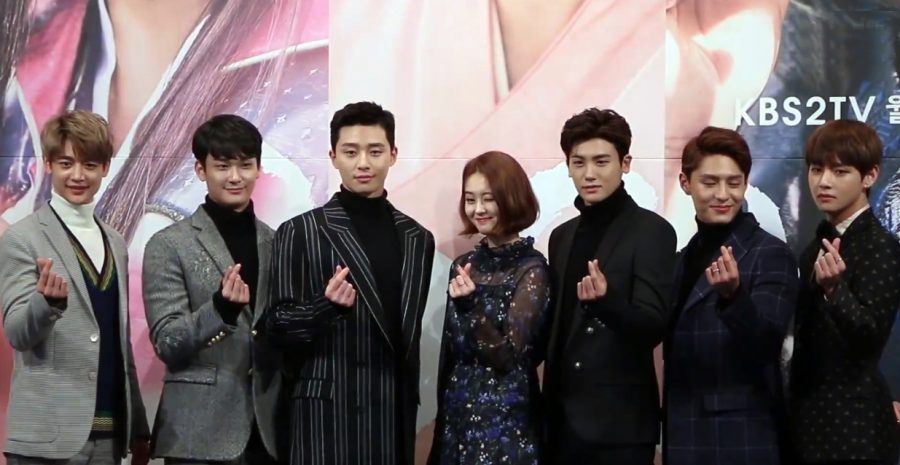 The cast of Hwarang, consisting of numerous famous idols and actors, pose for heart picture at a conference. 