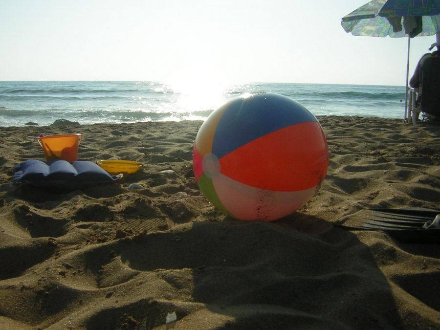A beach ball is resting peacefully with the sun behind it on the beach.