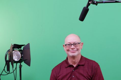 Mr. Terrando sitting in his studio in front of his green screen that his students use to create the student news.